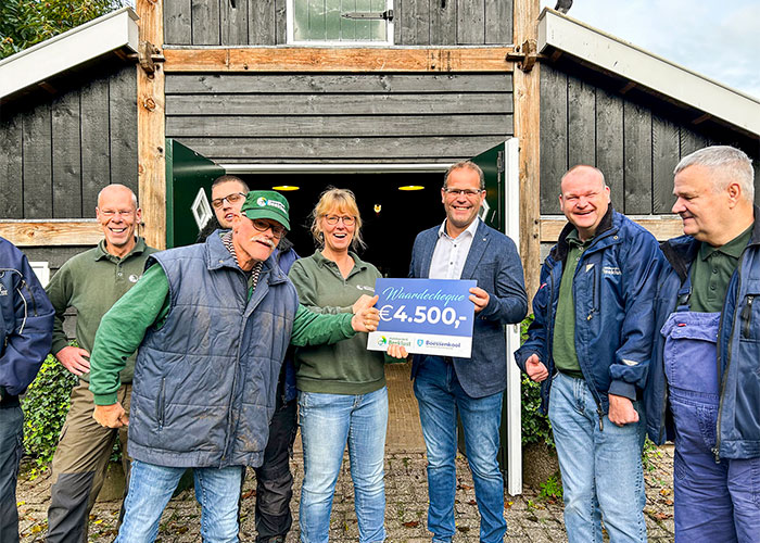 Omringd door deelnemers, neemt Gaby Bossink, Persoonlijk Begeleider bij Stadsboerderij Beeklust, de cheque in ontvangst uit handen van Eelco Osse van Machinefabriek Boessenkool.