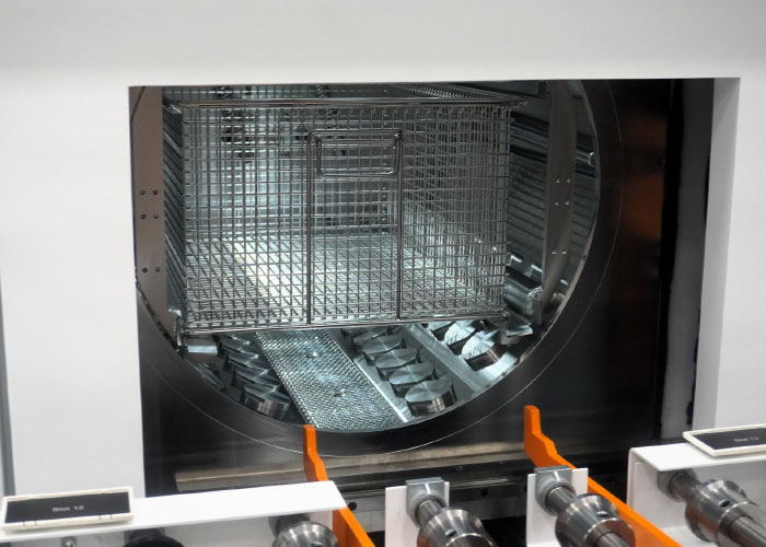 De manden met werkstukken worden automatisch aangevoerd in de reinigingsmachine. Na de reiniging worden de manden via een transportband en een sluis in de cleanroom gebracht. De foto toont duidelijk de ‘hockeypuck’-modules die zorgen voor een gelijkmatige verdeling van ultrasone energie.