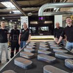 De 3 meter batchtafel aan de voorzijde van de SER1200 Multibrush maakt batchgewijs finishen mogelijk. Links de Zuidberg medewerkers. V.l.n.r. Toon van Steenoven, manager process engineering, Kenroy Simmons, operator, en Alwin Boer, teammanager snijden, kanten en nabewerking. Rechts van de tafel Patrick van Scherpenseel en Stef van der Zanden van Q-Fin.